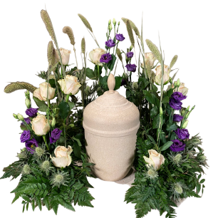 En urna omgiven av ljusa och lila rosor samt gröna blad och gräs.