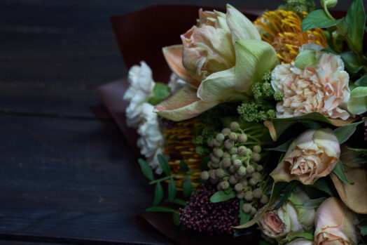 En bukett med blandade blommor och gröna växter på ett mörkt bord.