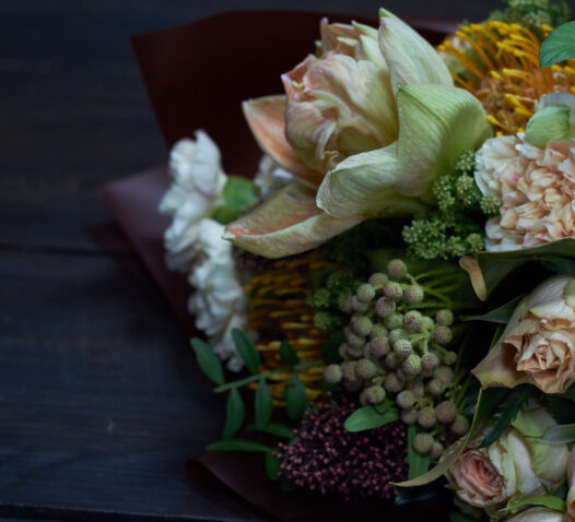 En bukett med blandade blommor och gröna växter på ett mörkt bord.
